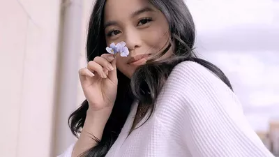 Model with dark hair holding a white flower