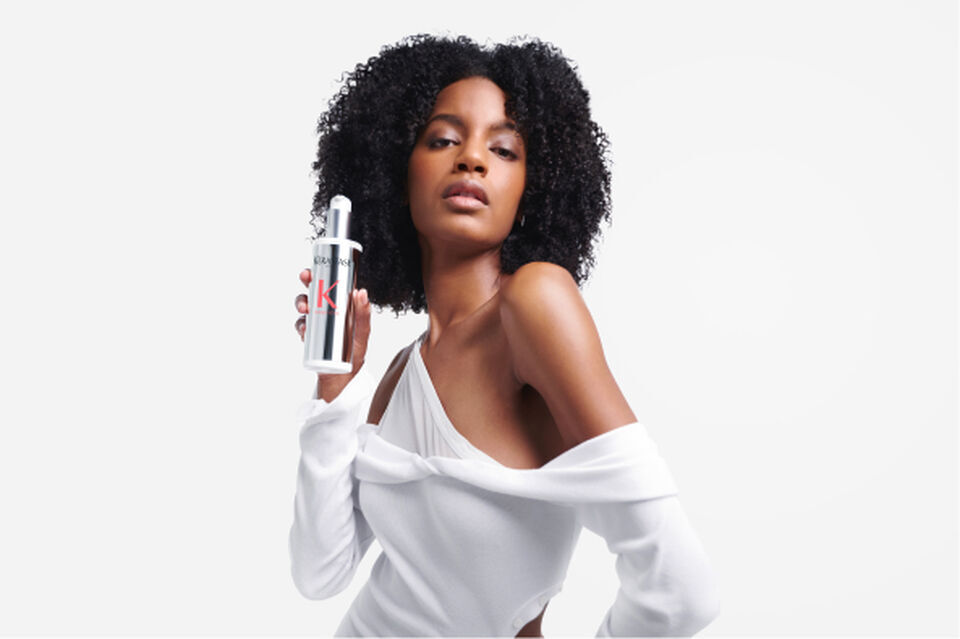 Model with dark curly hair holding a bottle of Premiere Decalcifying Repairing Treatment