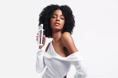 Model with dark curly hair holding a bottle of Premiere Decalcifying Repairing Treatment