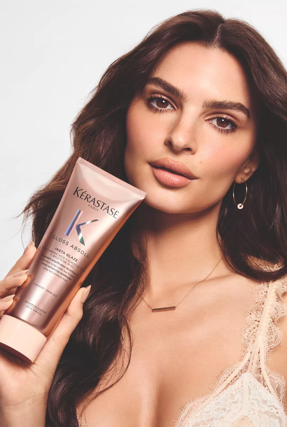 Model with long, smooth brown hair holding Kerastase Gloss Absolu conditioner