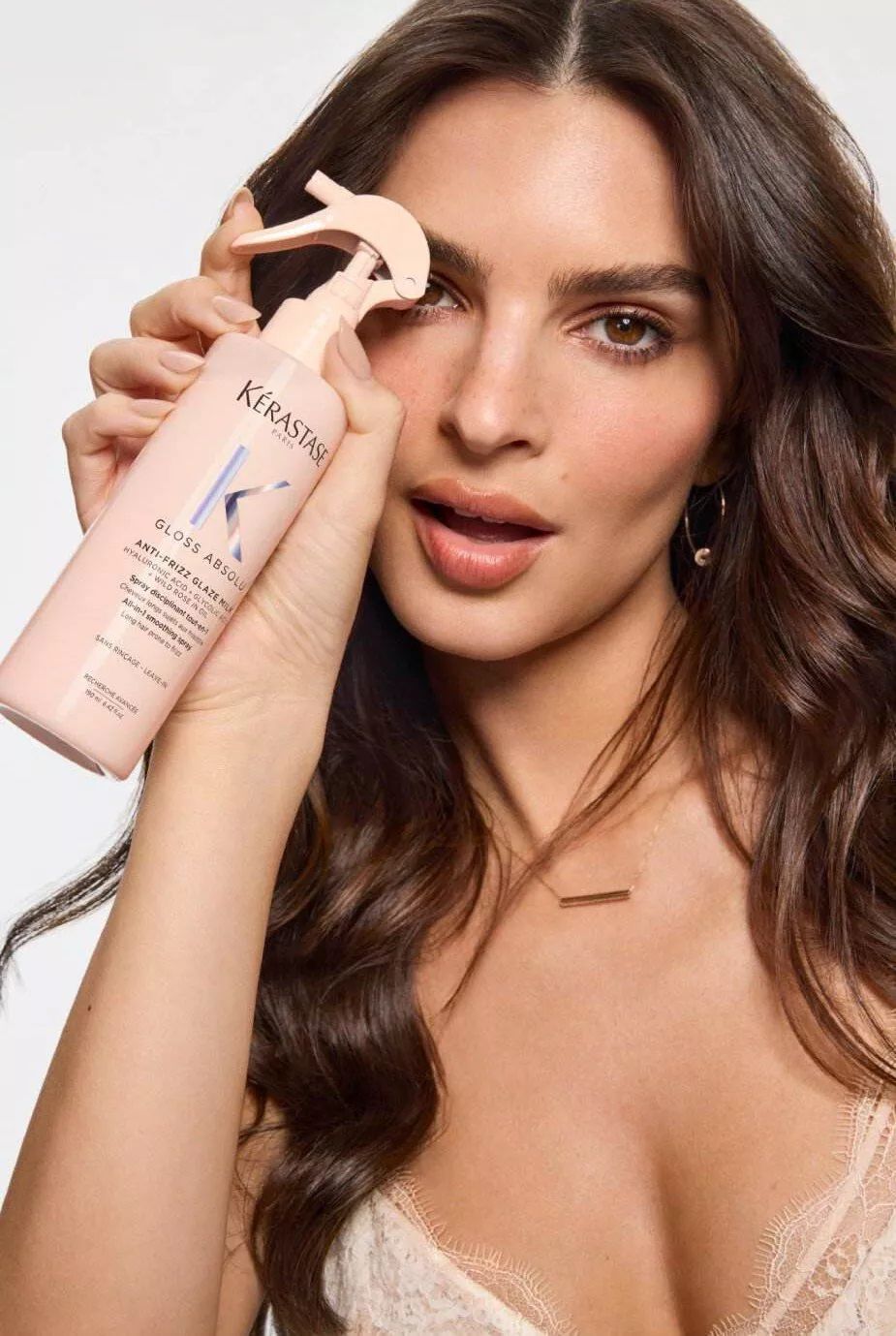 Model with long sleek brown hair holding the Kerastase Gloss Absolu Anti-Frizz Glaze Milk Smoothing Spray