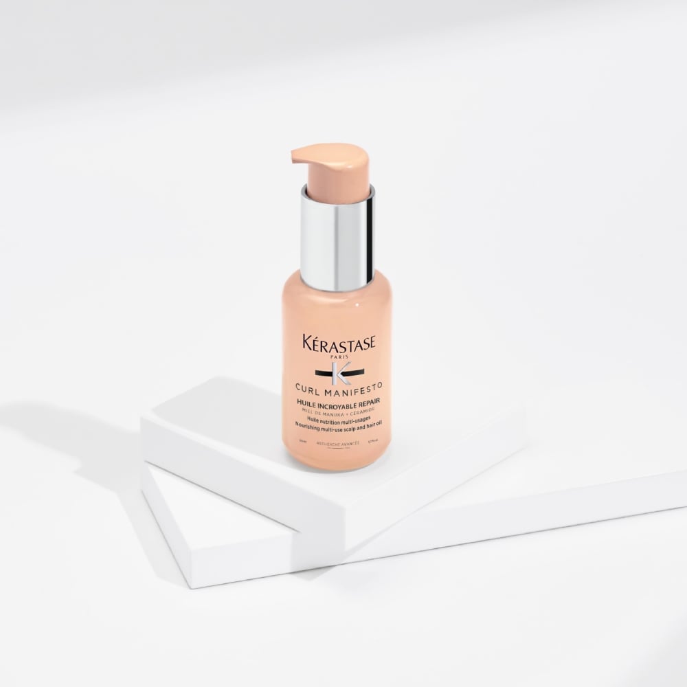 L’huile capillaire Curl Manifesto Huile Sublime Repair est présentée sur un fond gris épuré avec des cubes transparents. Cette huile hydrate et définit la forme des cheveux bouclés tout en réduisant les frisottis et les cassures.